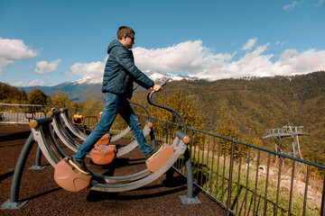 Naklejka premium Man uses outdoor exercise machine on mountain with snow-capped peaks