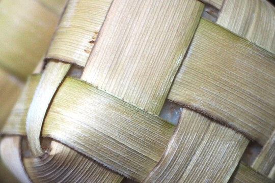 The pouch is made from interwoven strips of young coconut leaves , displaying natural textures, fine parallel lines, and slight color variations ranging from light