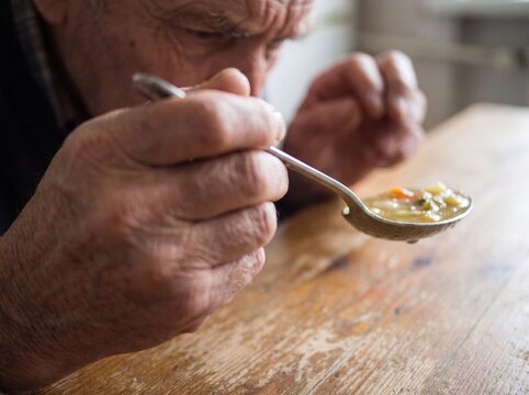A macro detail of a hand affected by Parkinson's disease trying to hold steady a spoon full of soup, the shaky camera movement following the rhythmic and uncontrollable tremor of the hand, highlightin