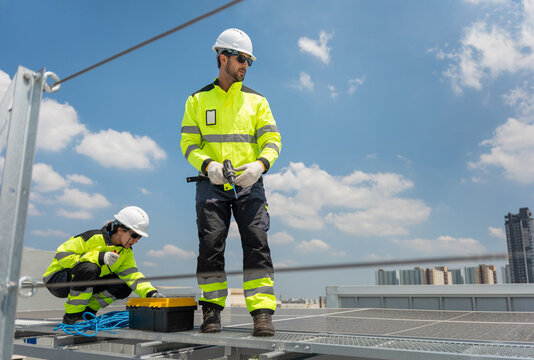 Team of engineer and maintenance worker in safety gear using power tools for installation solar panel projects, Solar technicians installing solar panels on industrial rooftop