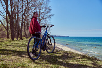 Fototapeta premium Young woman standing with bicycle near seaside under clear blue sky in sunny outdoor setting