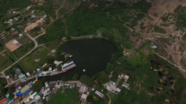 Top-down aerial view of the sacred Gopi Talav lake surrounded by lush green forest near Dwarka, Gujarat.