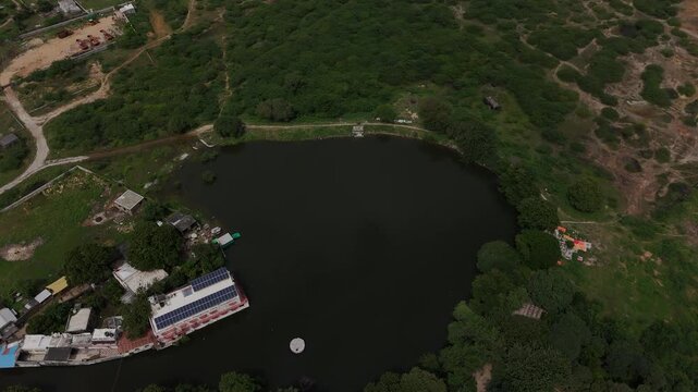 Top-down aerial view of the sacred Gopi Talav lake surrounded by lush green forest near Dwarka, Gujarat.