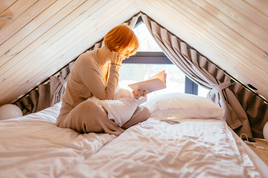 Mature Woman Reading Book In Loft Bed Under Warm Morning Light