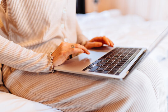 Close Up Of Mature Woman Typing On Laptop While Relaxing In Bed