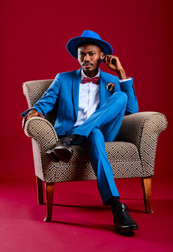 Confident man wearing blue suit sitting on chair against red background