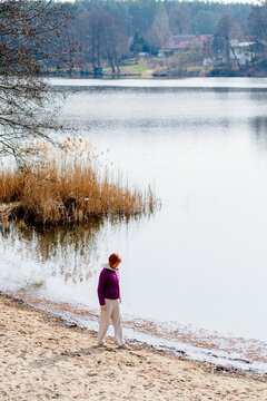Mature Woman Walking Along Lakeshore During Nature Retreat Vertical
