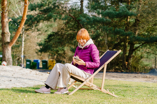 Mature Woman Using Smartphone While Relaxing On Deck Chair Outdoors