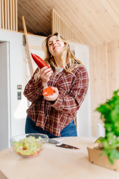 Playful Young Woman Holding Sweet Pepper While Making Salad