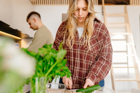 Young Woman Preparing Fresh Vegetables While Partner Cooks In Modern Cabin