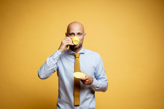 Portrait of bald businessman drinking cup of coffee against yellow background