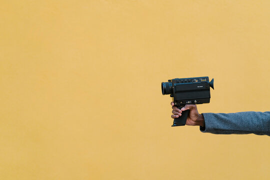 Man holding 1980s camera against yellow wall