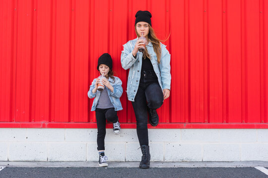 Teenage girl and little sister leaning against red wall drinking cocoa