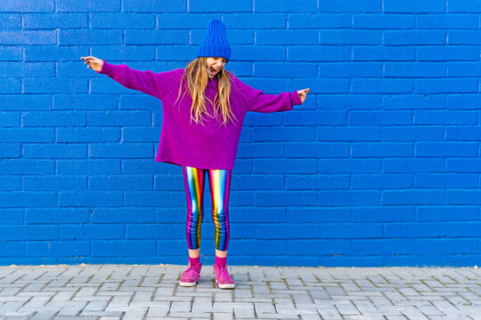 Girl wearing blue cap and oversized pink pullover standing in front of blue wall singing