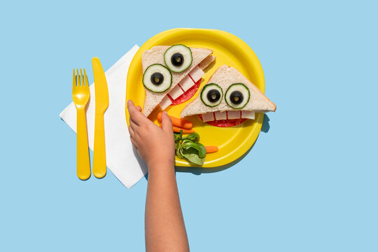 Hand of baby girl picking up funny looking sandwich with anthropomorphic face