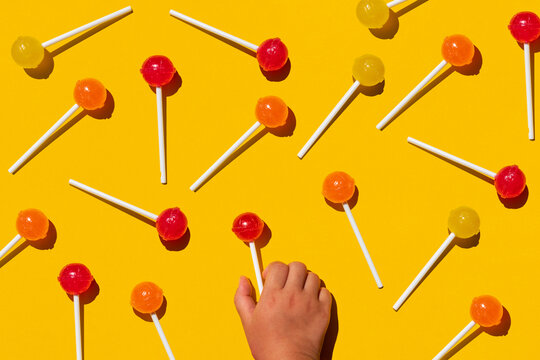 Studio shot of hand of baby girl picking up one of lollipops lying against yellow background