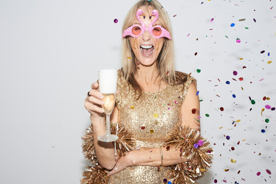 Senior woman wearing golden dress and flmingo shaped glasses, celebtraing New Year's Eve