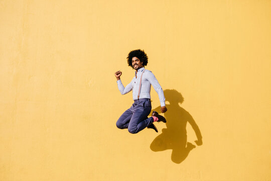 Smiling man jumping in the air in front of yellow wall