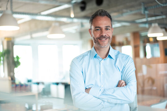 Smiling businessman standing with arms crossed at workplace