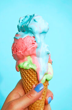Woman's hand holding ice-cream cone with melting icecream in front of blue background
