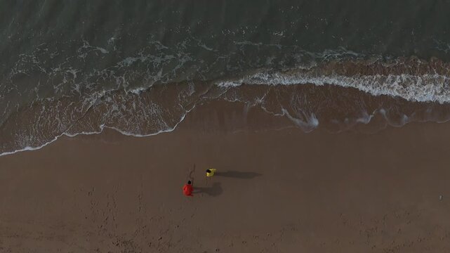 Cinematic high-angle aerial view of the word "Dwarka" written in Hindi on the sea beach sand as ocean waves approach.