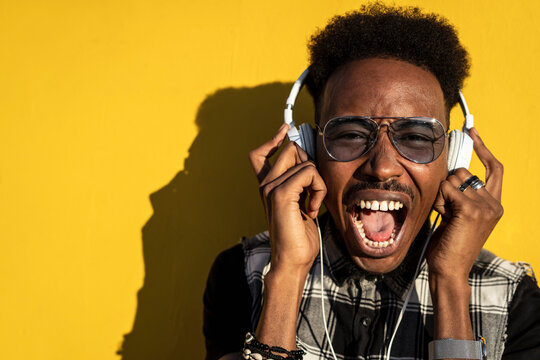 Portrait of screaming young man against yellow wall listening favourite song with headphones