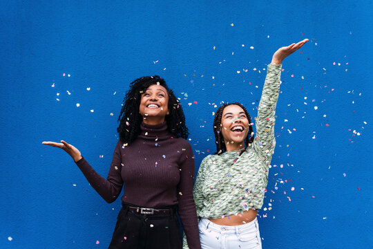 Happy friends throwing confetti standing in front of blue wall