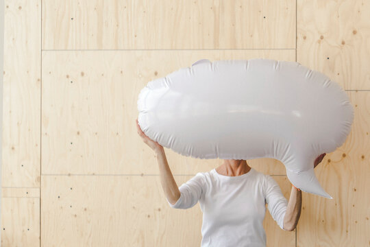 Woman standing in office, holding inflatable speech bubble in front of her face