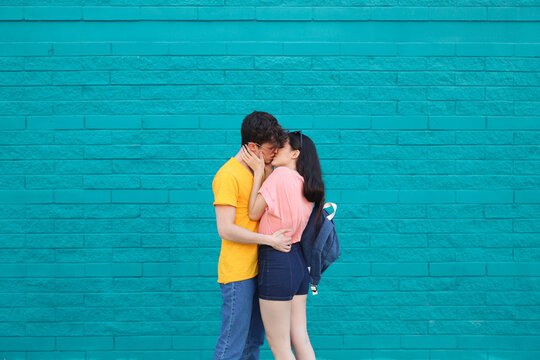 Young couple kissing in front of blue brick wall