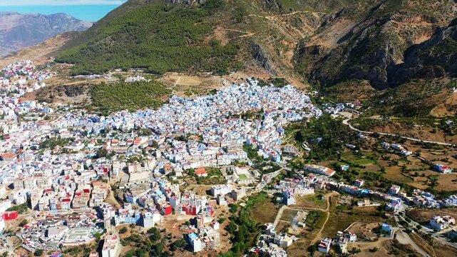 Drone aerial view of the blue city of Chefchaouen surrounded by dramatic Rif Mountains in northern Morocco. Scenic urban landscape ideal for travel and documentary projects.
