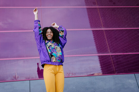 Young woman with urban look cheering in front of pink glass wall