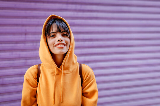 Portrait of young woman with yellow hoodie in front of purple background