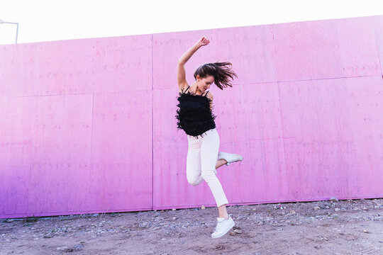 Exuberant young woman jumping in front of pink wall
