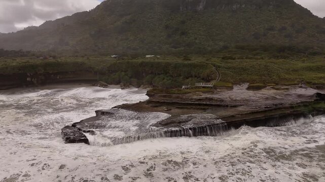 Ocean waves rushing over rocks at Truman Track in west coast of South Island of New Zealand, drone tracking shot