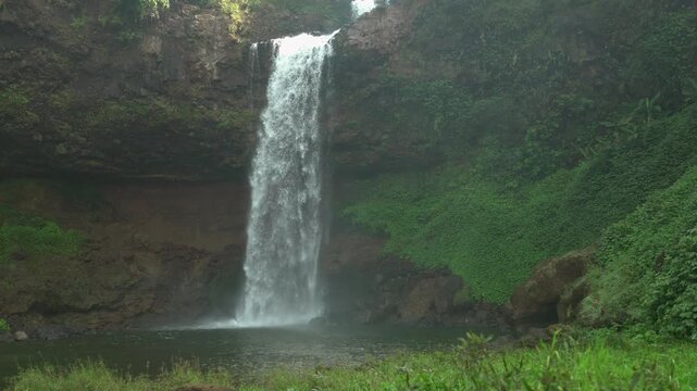 Static slow motion shot of Tad E-Tu waterfall plunging from a rocky cliff into a misty pool on the Bolaven Plateau in Laos.