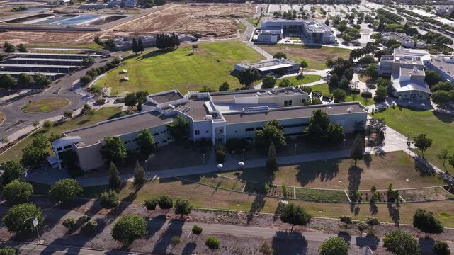 Drone perspective slowly orbiting the modern campus buildings and green lawns of Clovis Community College in Fresno, California, showcasing the academic and educational environment