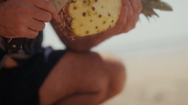 Hands slicing fresh pineapple with a large knife outdoors