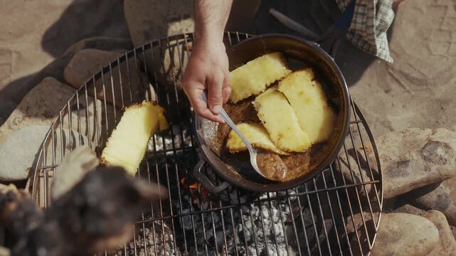 Cooking pineapple slices in a cast iron pan over a campfire