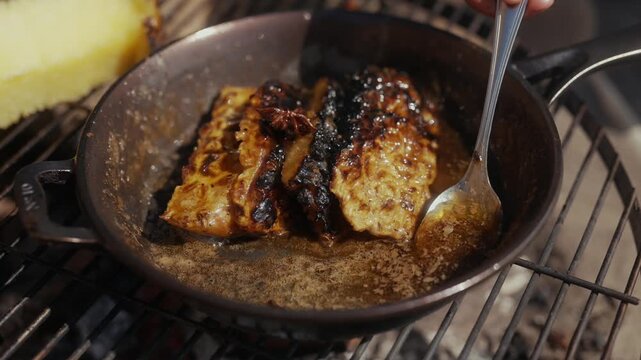 Spoon basting food in a cast iron pan on a grill