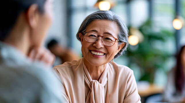A Japanese senior businesswoman smiles warmly while interviewing a calm young candidate in a bright modern office in soft daylight candidate interview open face modern office