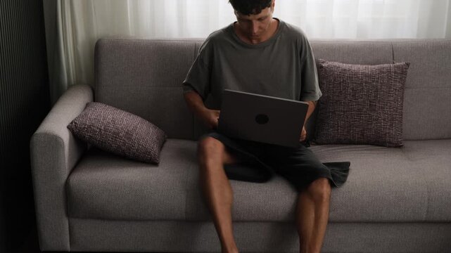 Remote worker changing positions around apartment while working on laptop, authentic freelance routine and modern digital lifestyle in small living space