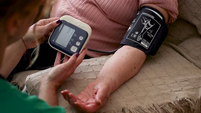 Nurse measuring blood pressure of elderly woman at home. Home healthcare visit, geriatric care, senior health monitoring, aging in place, medical assistance concept