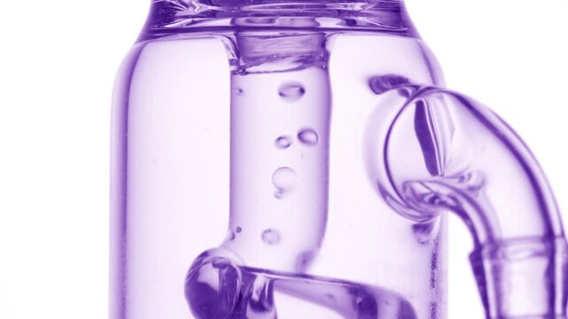Extreme close-up shot of bright clear fluid flowing through a glass tube, causing bubbles to condense and chaotically move inside it set over a white background
