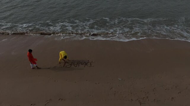 Cinematic high-angle aerial view of the word "Dwarka" written in English on the sea beach sand as ocean waves approach.