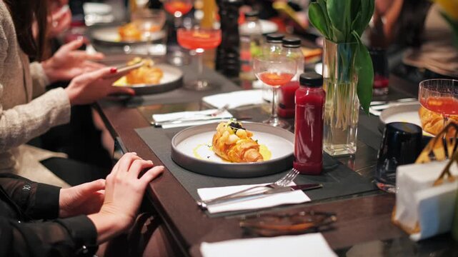 People photographing gourmet croissant dish with phones at elegant dinner table setting.