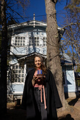 Obraz premium happy, contented woman holds a birthday cake and smiles, having party in nature.chocolate cake is decorated with icing burning candle. person is standing in park and enjoying anniversary celebration. 