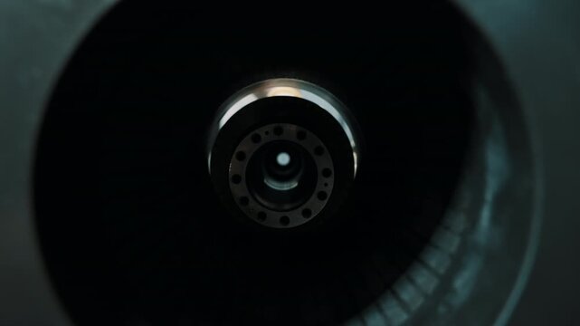 Industrial close-up through a cylindrical housing at a machined rotor assembly, as a technician aligns the metal component in a workshop fixture for inspection.