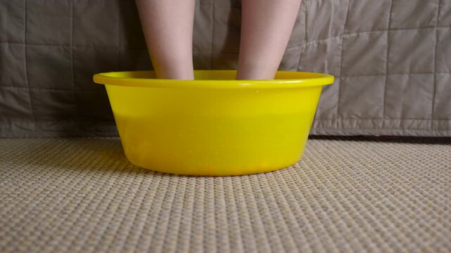 Woman soaking tired feet in a basin of water. Woman feet soaking in a yellow basin of warm water as part of a relaxing home spa treatment and pedicure routine, relieving aches and providing comfort