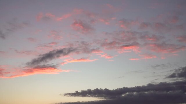 Gentle cloud layers move across a warm-toned evening sky as sunset colors blend in calm atmospheric motion. Ideal for weather themes, tranquil mood projects, or cinematic nature scenes. 