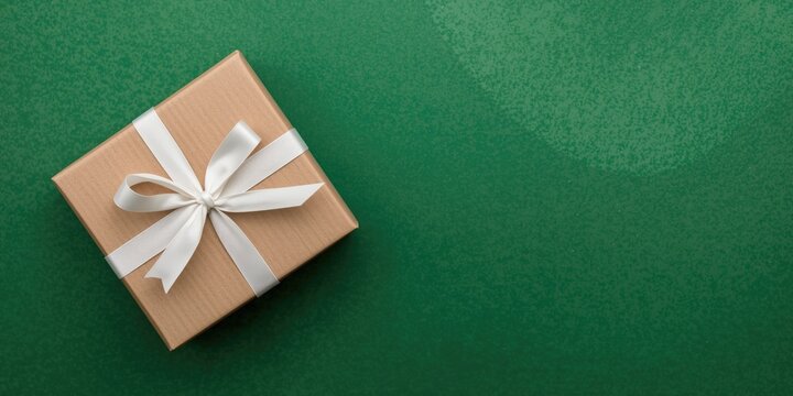 Handmade holiday gift box tied with white ribbon on a green festive textured background